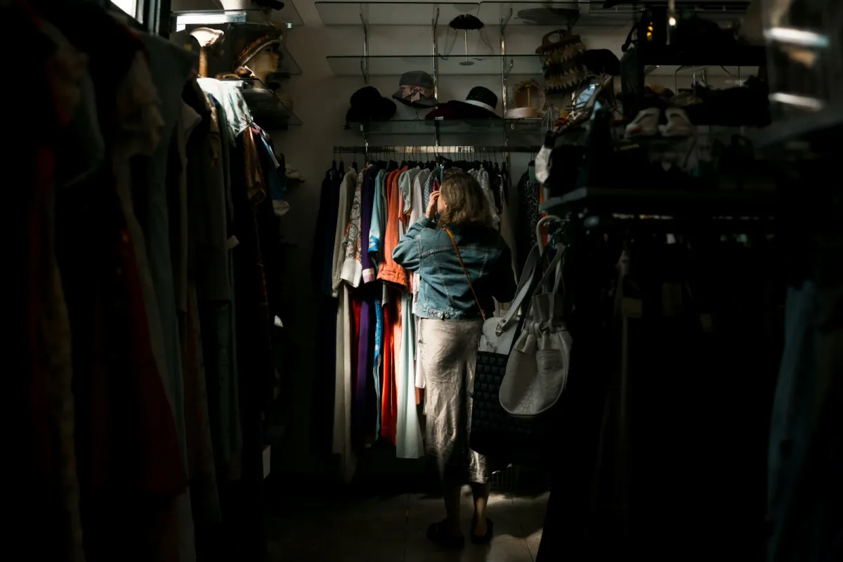 A shopper seen from behind browsing a rail of colourful clothes in a dimly lit boutique