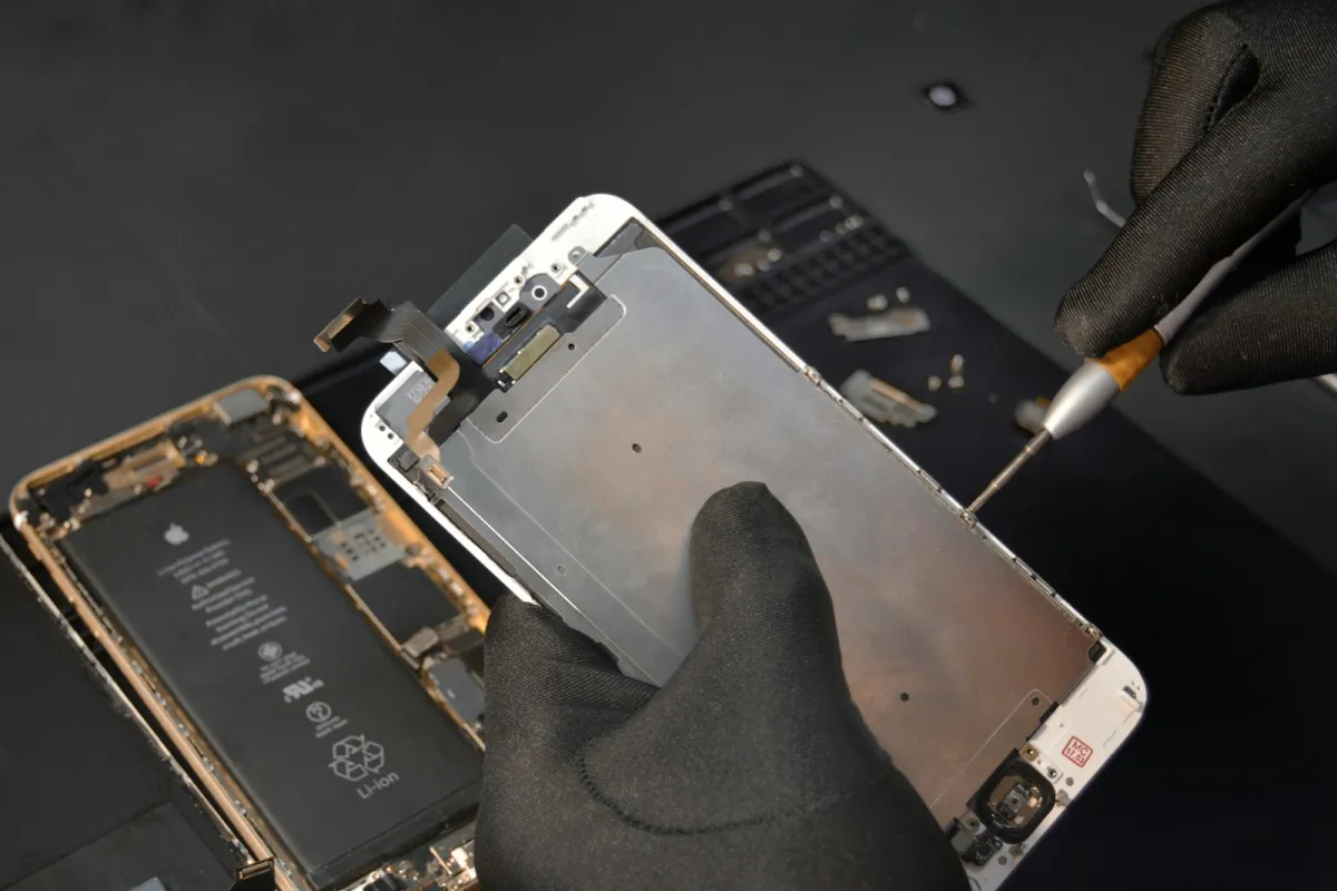 Gloved hands using a screwdriver to take apart a smartphone on a repair mat
