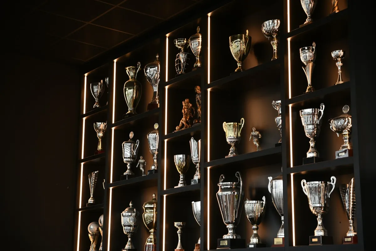 Rows of silver and gold sports trophies on lit display shelves