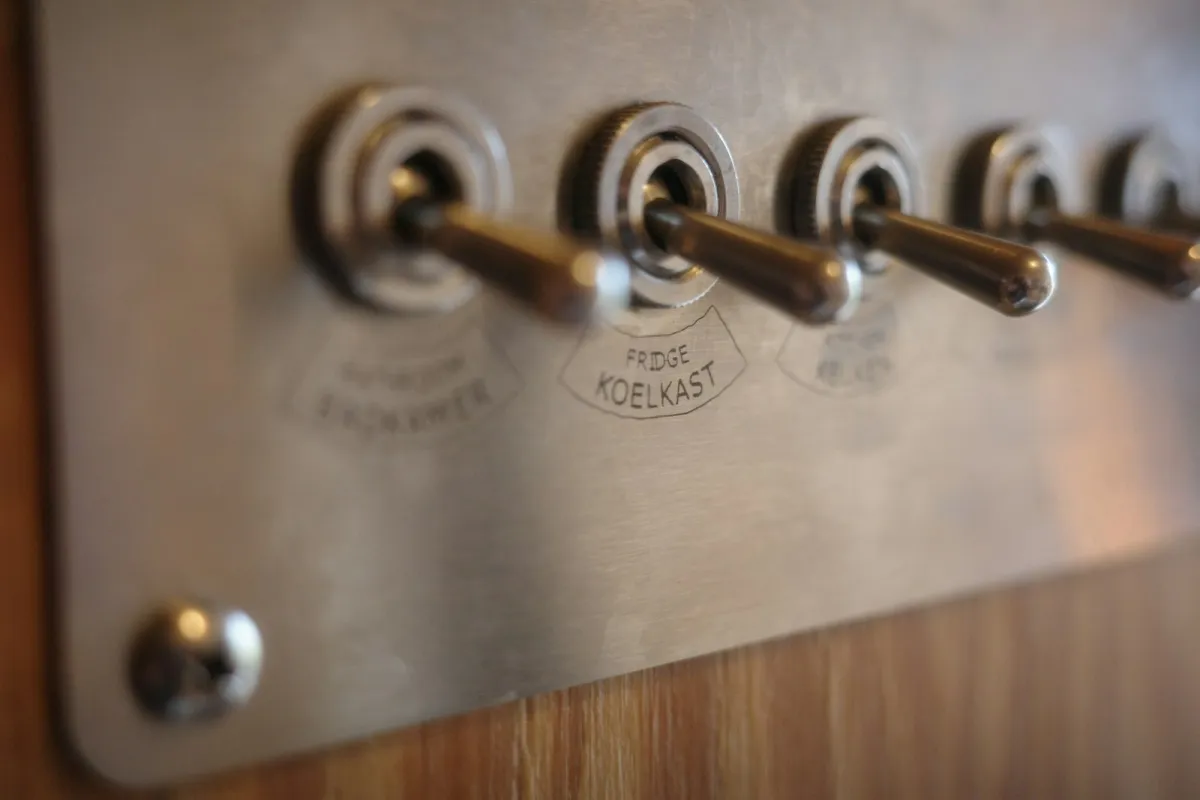 A row of metal toggle switches on a brushed steel plate mounted on a wooden wall A row of metal toggle switches on a brushed steel plate mounted on a wooden wall