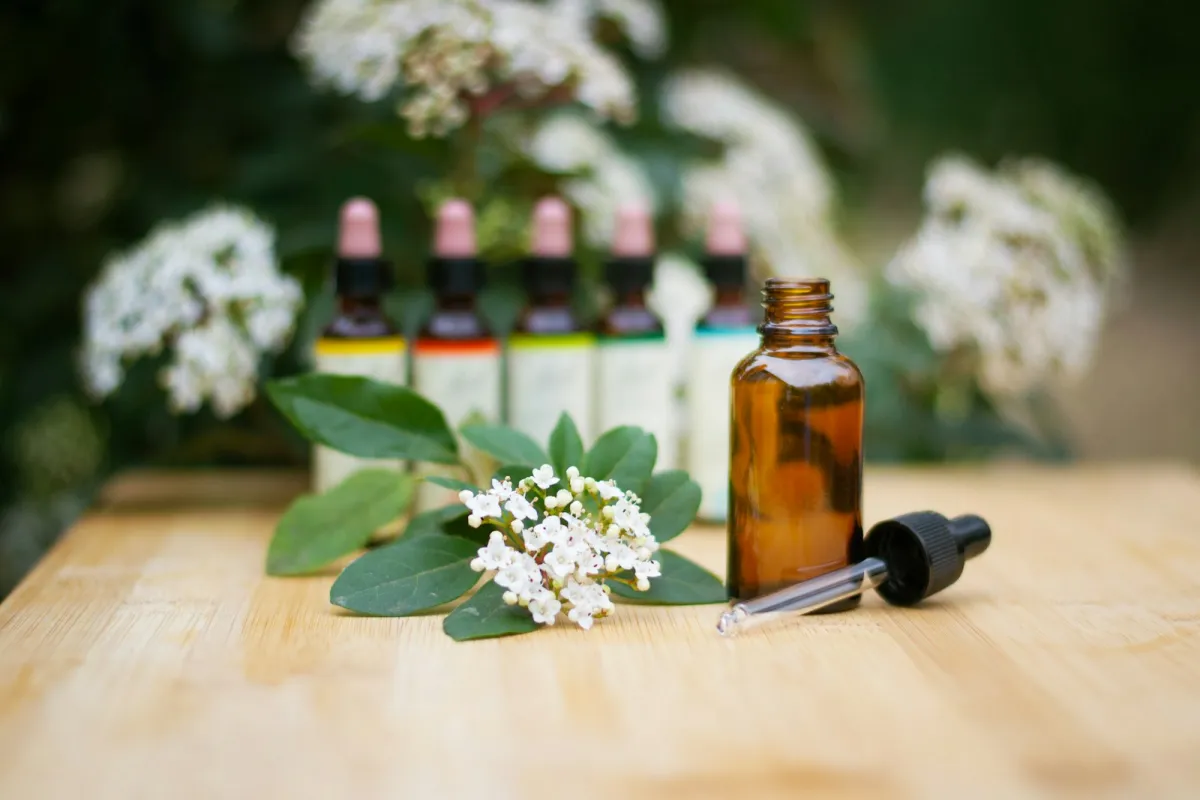 An amber glass dropper bottle beside a sprig of white flowers on a wooden table An amber glass dropper bottle beside a sprig of white flowers on a wooden table