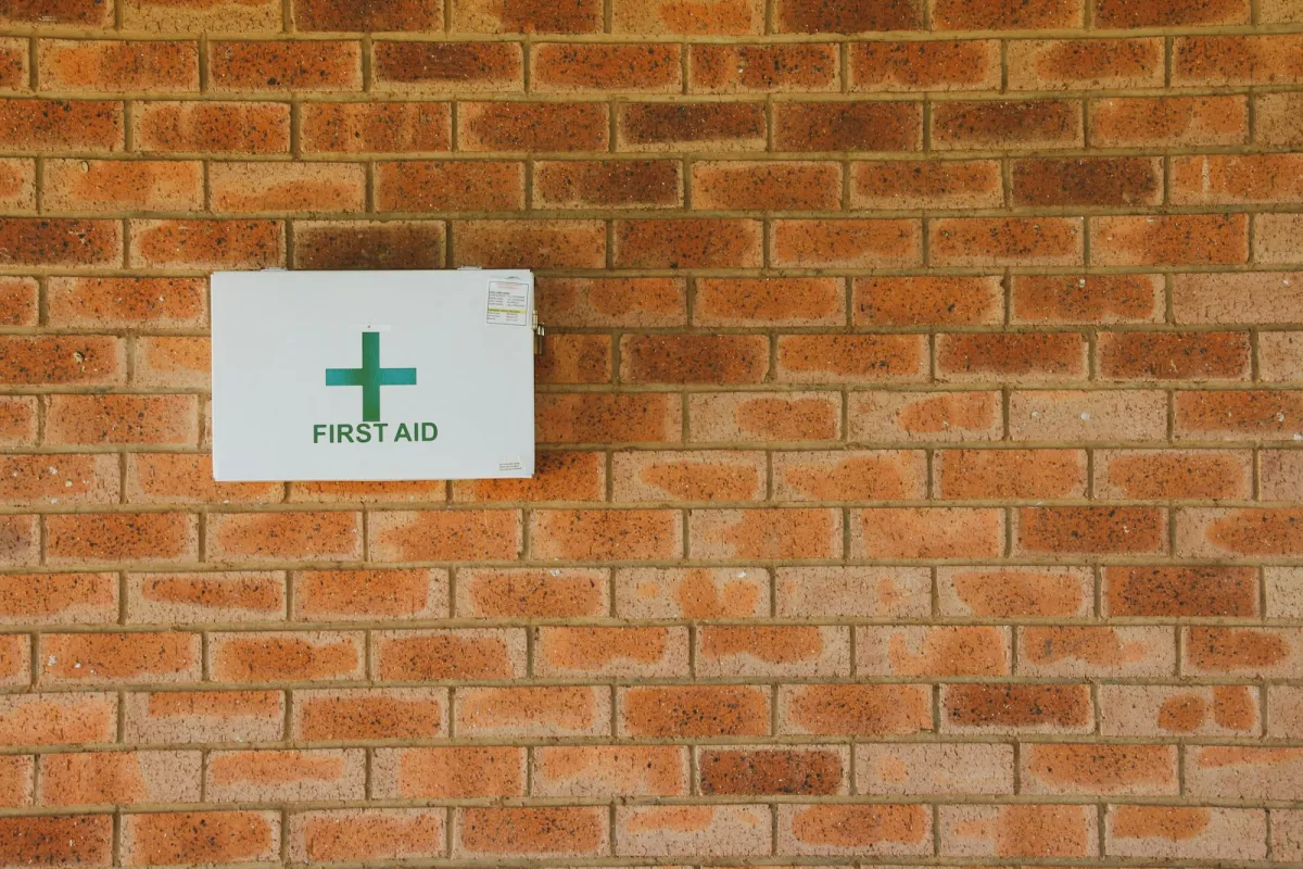 A white first aid box with a green cross mounted on a brick wall