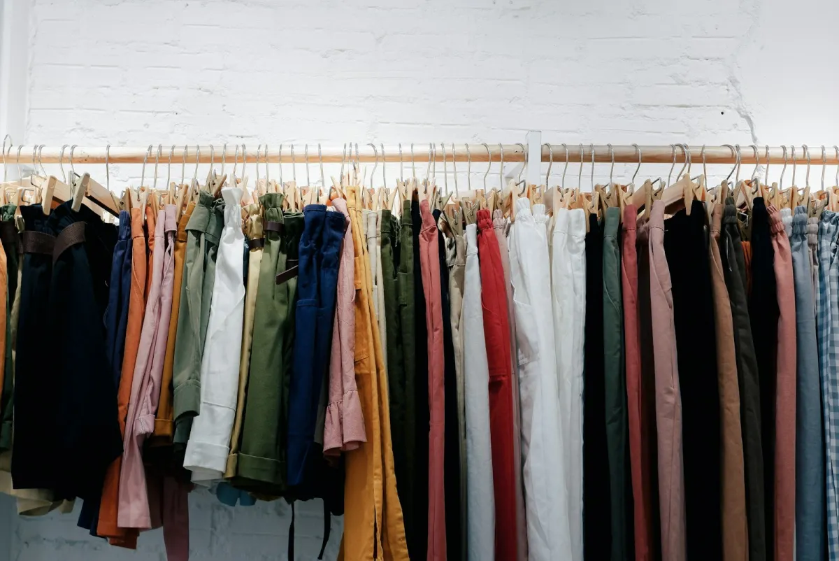 Rail of colourful clothes on wooden hangers against a white brick wall