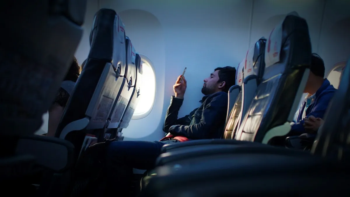 Passenger in a window seat on a plane looking at a smartphone