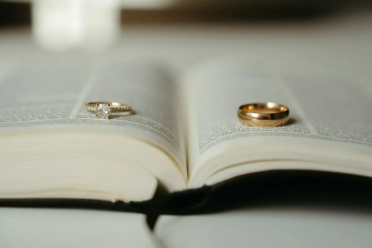 An engagement ring and a gold wedding band resting on the pages of an open book An engagement ring and a gold wedding band resting on the pages of an open book
