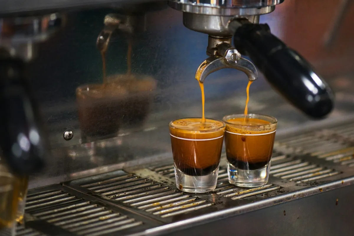 Two shots of espresso pouring from a portafilter into small glasses on a machine drip tray