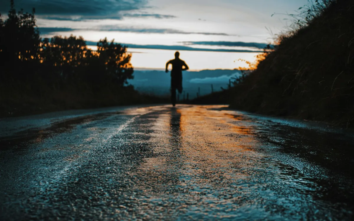 Silhouette of a runner on a wet country road at sunset Silhouette of a runner on a wet country road at sunset