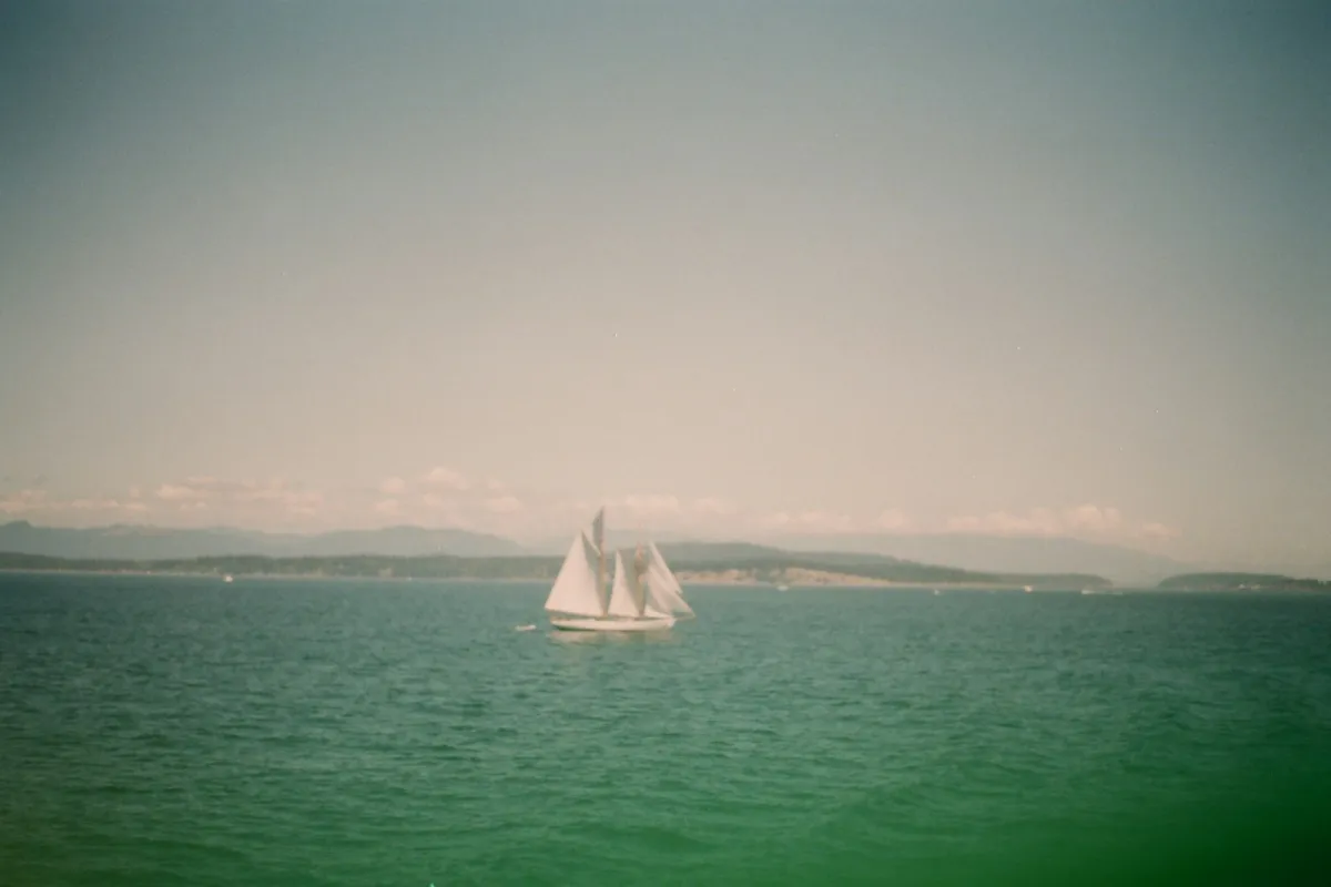 A white-sailed schooner sailing across green water with hills on the horizon