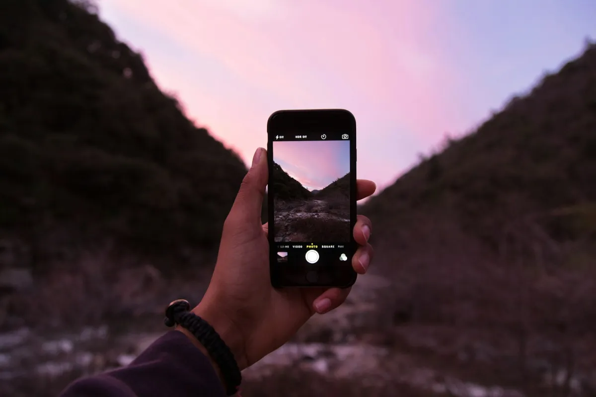 Hand holding a smartphone with its camera app open against a pink evening sky Hand holding a smartphone with its camera app open against a pink evening sky
