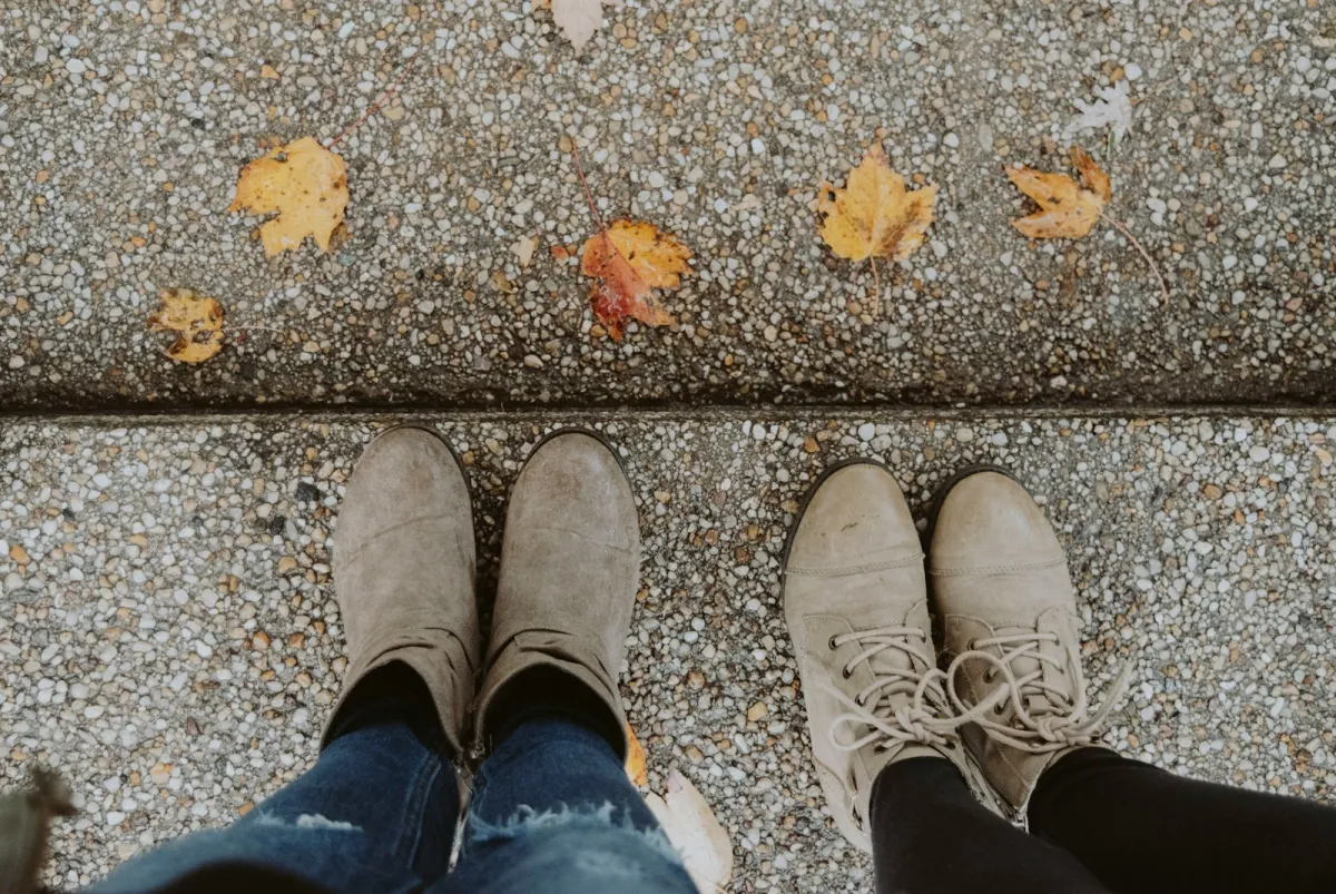 Two pairs of suede ankle boots on a pavement scattered with autumn leaves Two pairs of suede ankle boots on a pavement scattered with autumn leaves