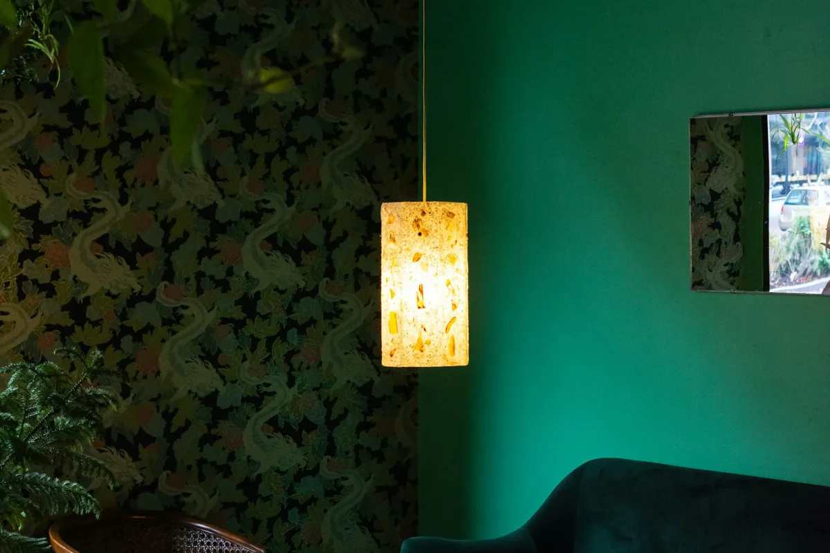 A paper pendant lamp glowing in a room with dark patterned wallpaper on one wall and a green painted wall