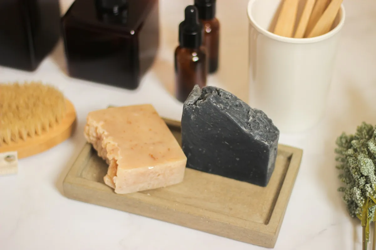 Two bars of handmade soap on a stone soap dish beside a wooden brush