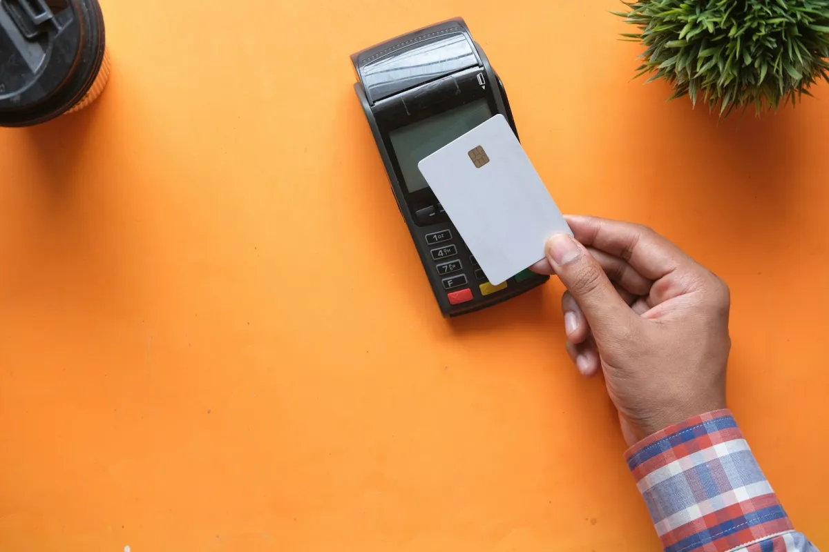 Hand holding a blank card next to a card payment terminal on an orange table
