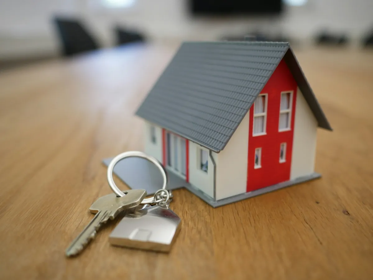 A small wooden model house on a table, with keys beside it A small wooden model house on a table, with keys beside it