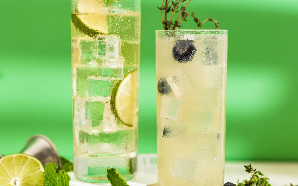 Two tall iced drinks with lime, blueberries and thyme