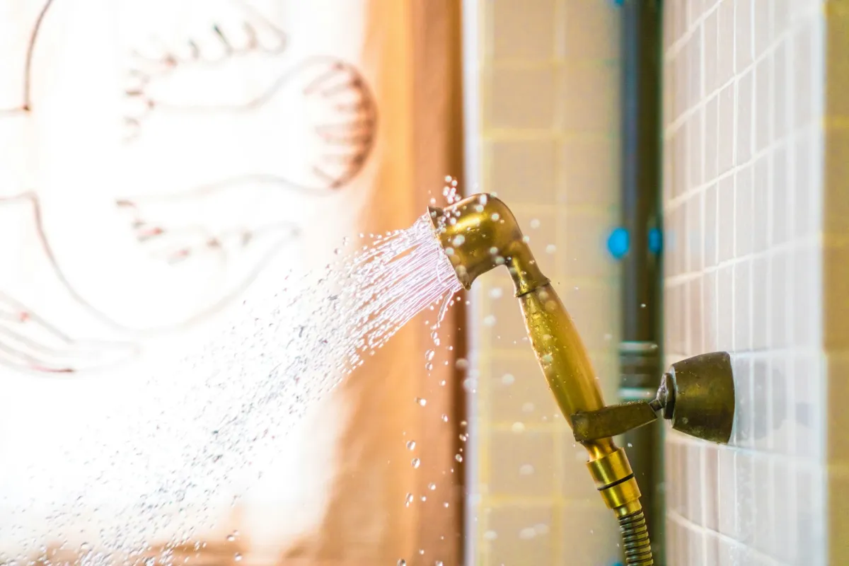 A brass handheld shower head spraying water beside a tiled wall A brass handheld shower head spraying water beside a tiled wall