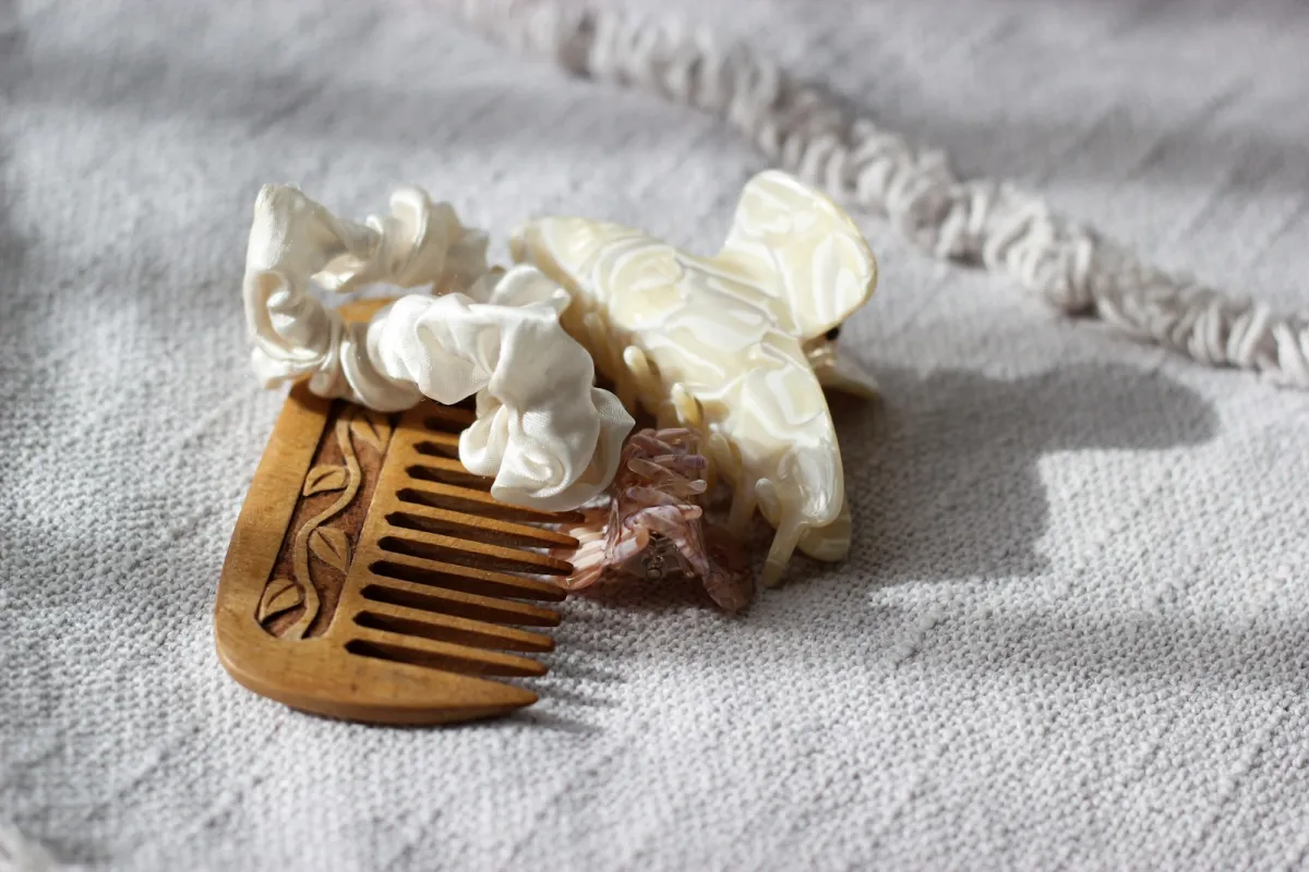 A wooden comb with cream scrunchies and a hair clip on grey linen A wooden comb with cream scrunchies and a hair clip on grey linen