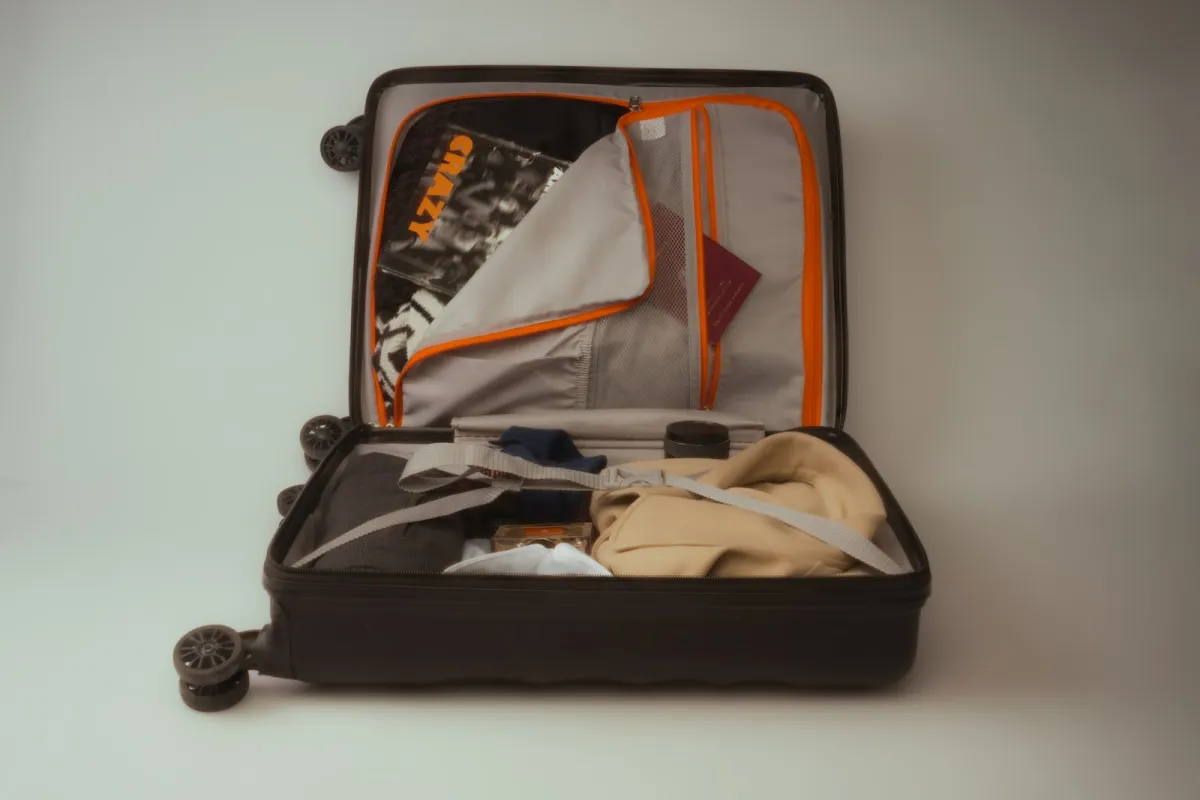 An open black suitcase packed with clothes and a passport for a trip