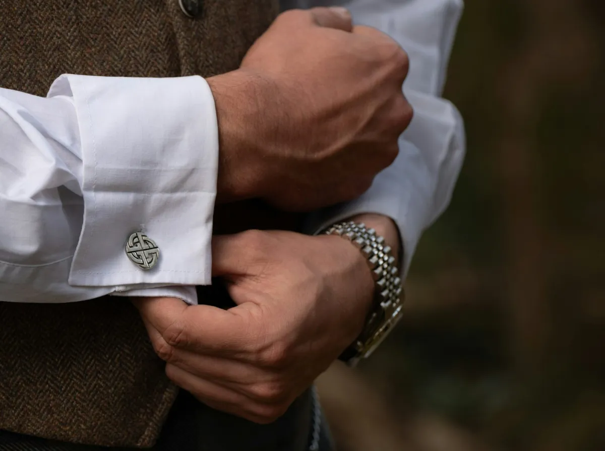 A man fastening a silver cufflink on a white double-cuff shirt A man fastening a silver cufflink on a white double-cuff shirt