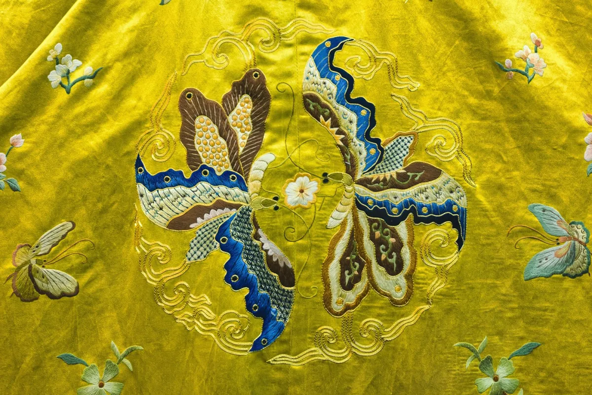 Close-up of yellow silk with hand-embroidered butterflies and flowers Close-up of yellow silk with hand-embroidered butterflies and flowers