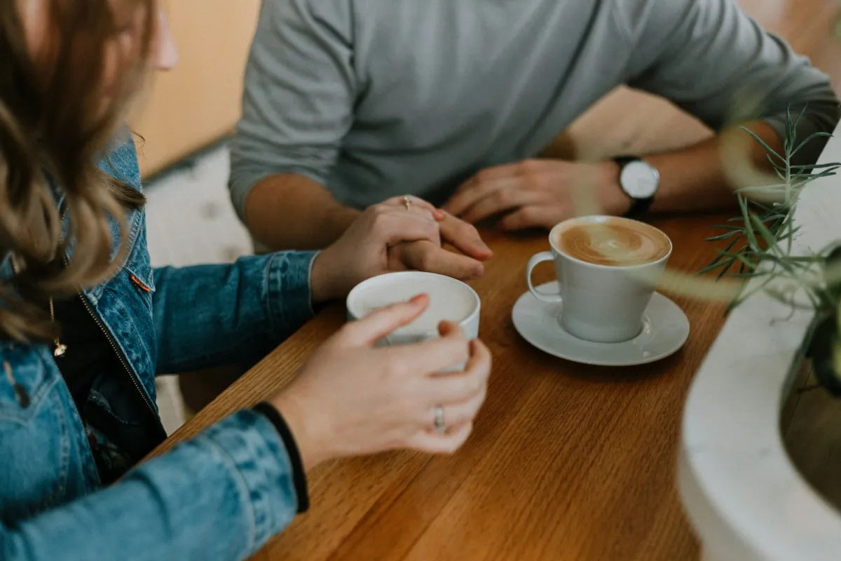 Two people holding hands across a café table beside two cups of coffee Two people holding hands across a café table beside two cups of coffee