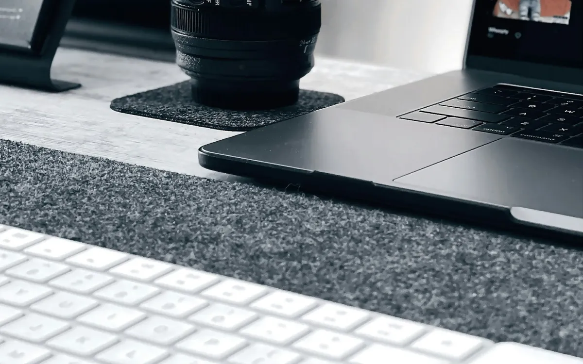 A camera lens on a felt coaster beside a laptop and keyboard on a desk
