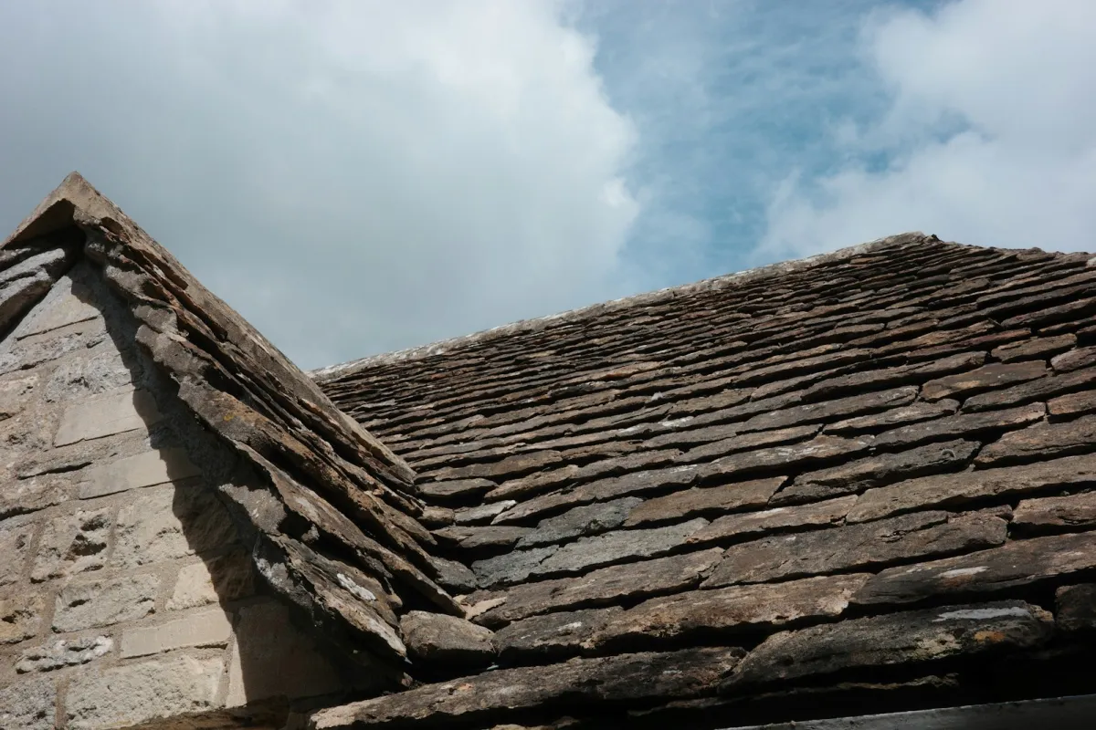 Weathered stone roof tiles under a cloudy blue sky