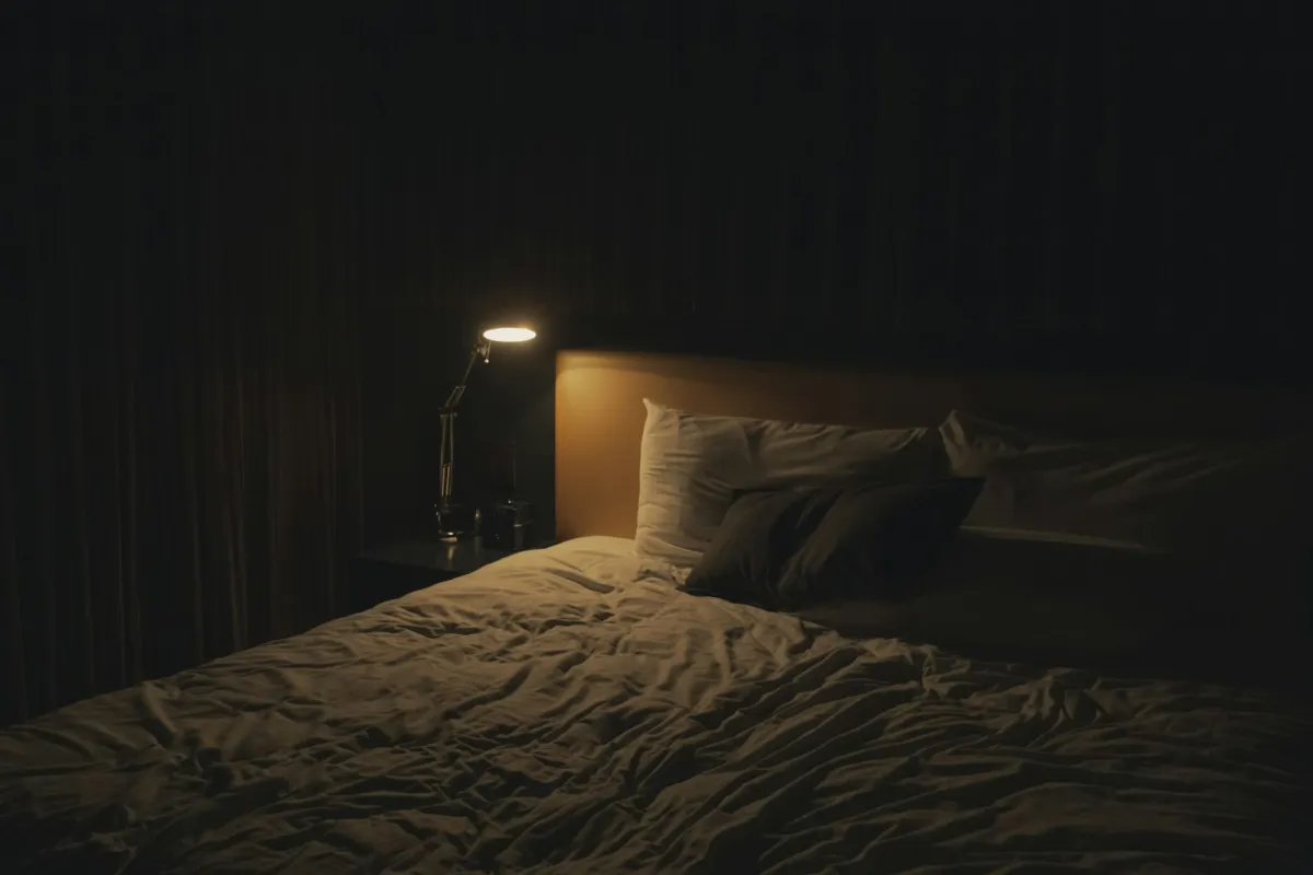 Bedside table lamp glowing next to a made bed