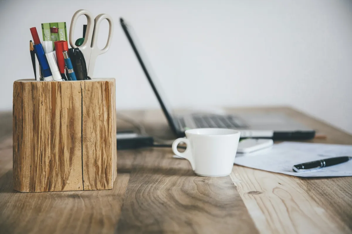 White cup on a wooden desk beside a pen pot and laptop