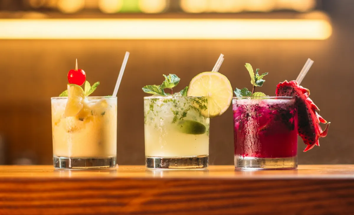 Three colourful cocktails garnished with mint, lime and fruit lined up on a wooden bar Three colourful cocktails garnished with mint, lime and fruit lined up on a wooden bar