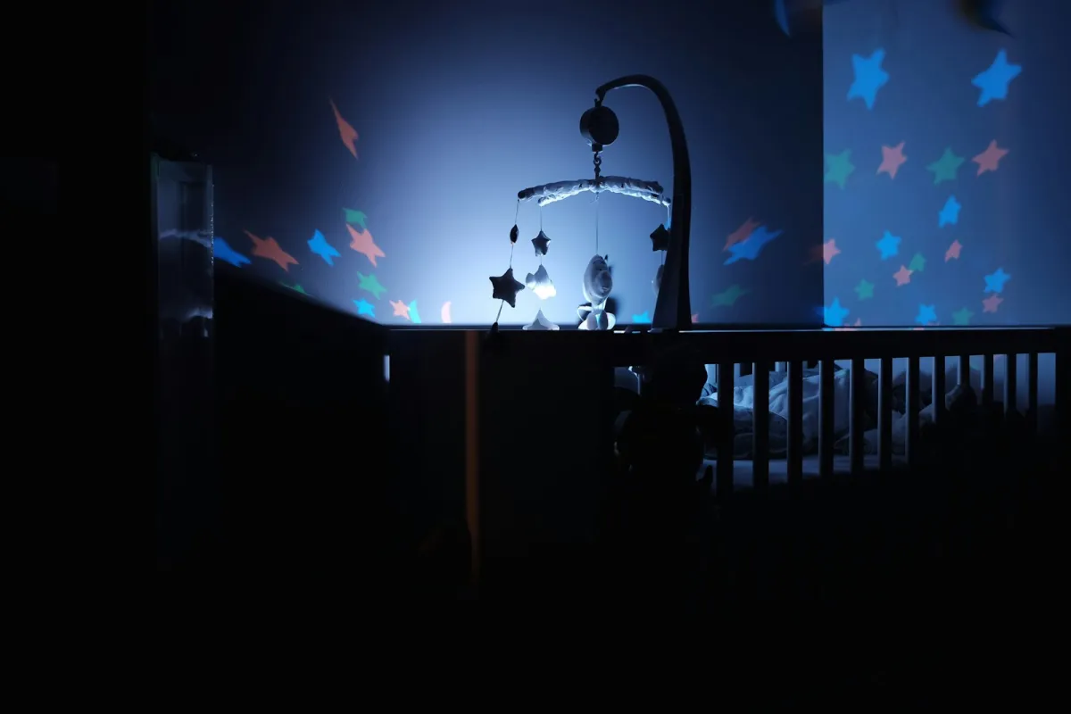 A dark nursery with a cot, a mobile and star shapes projected on the wall A dark nursery with a cot, a mobile and star shapes projected on the wall