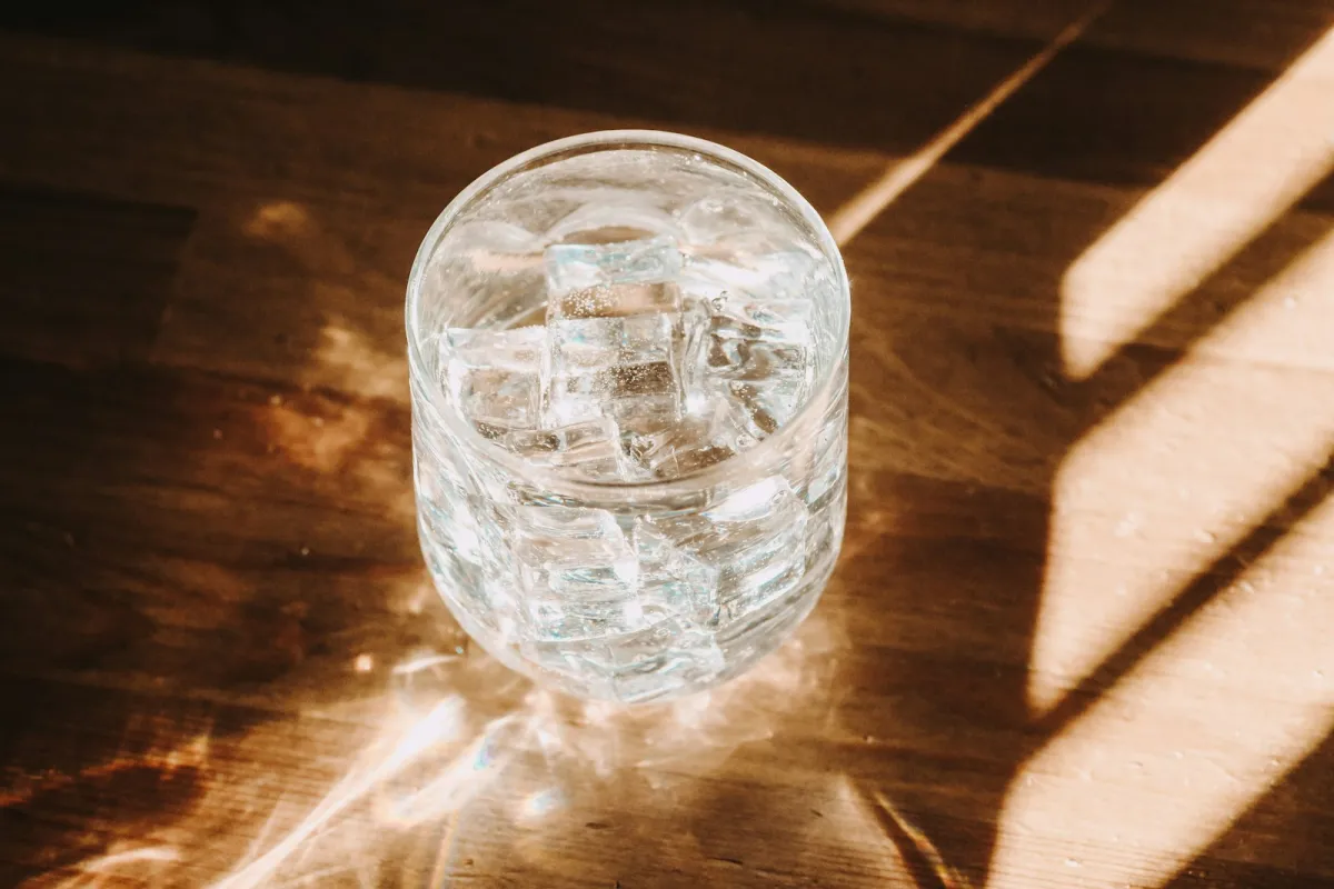 A glass of sparkling water with ice on a sunlit wooden table A glass of sparkling water with ice on a sunlit wooden table