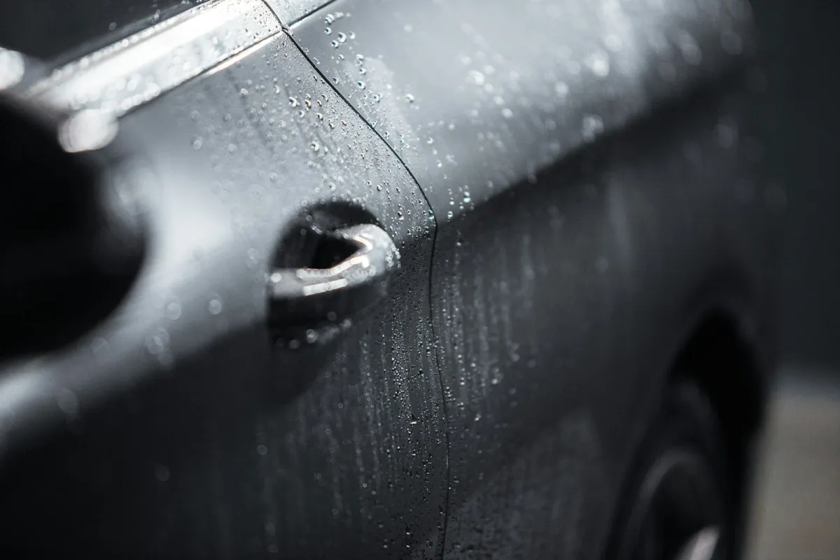 Close-up of rain droplets on the door and handle of a dark car