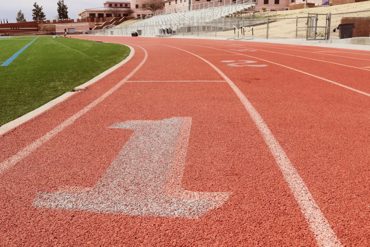 Lane one of a red running track beside a sports pitch