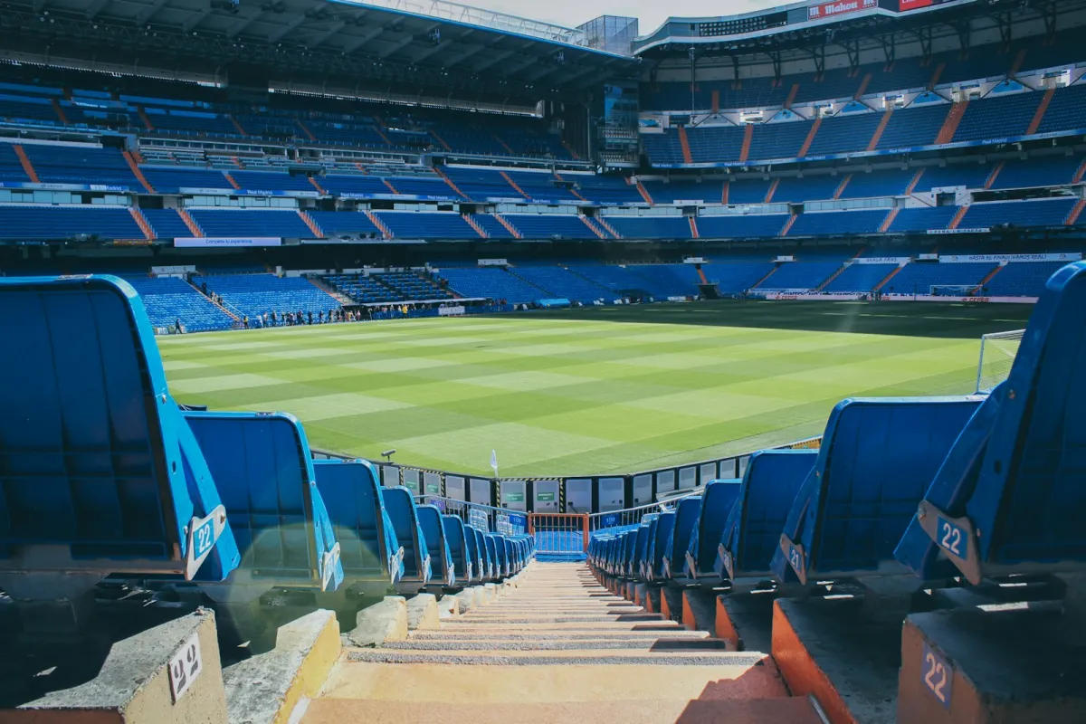 Rows of empty blue seats leading down to a football pitch in a large stadium Rows of empty blue seats leading down to a football pitch in a large stadium
