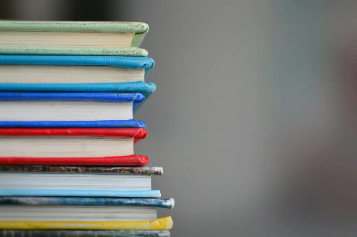 A tall stack of colourful hardback books against a grey background