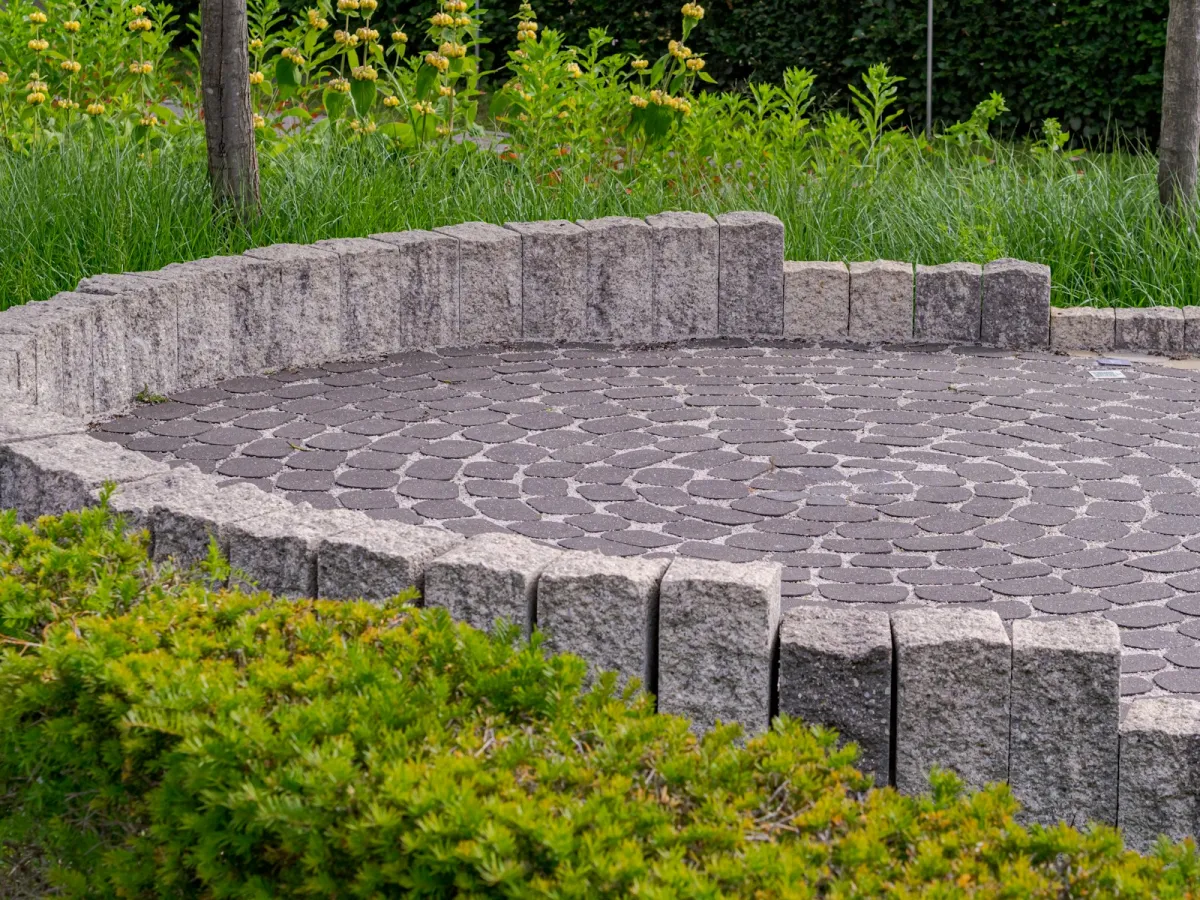 Circular paved patio edged by a low stone wall and green shrubs