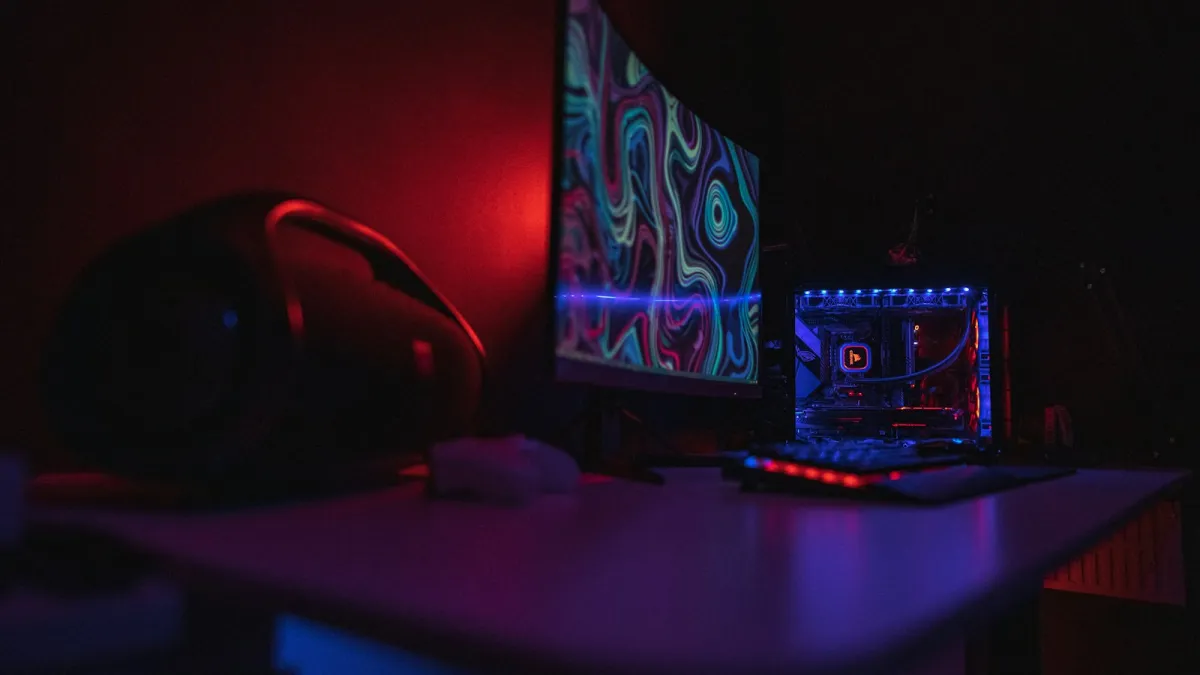 A gaming PC and curved monitor glowing red and blue on a desk in a dark room