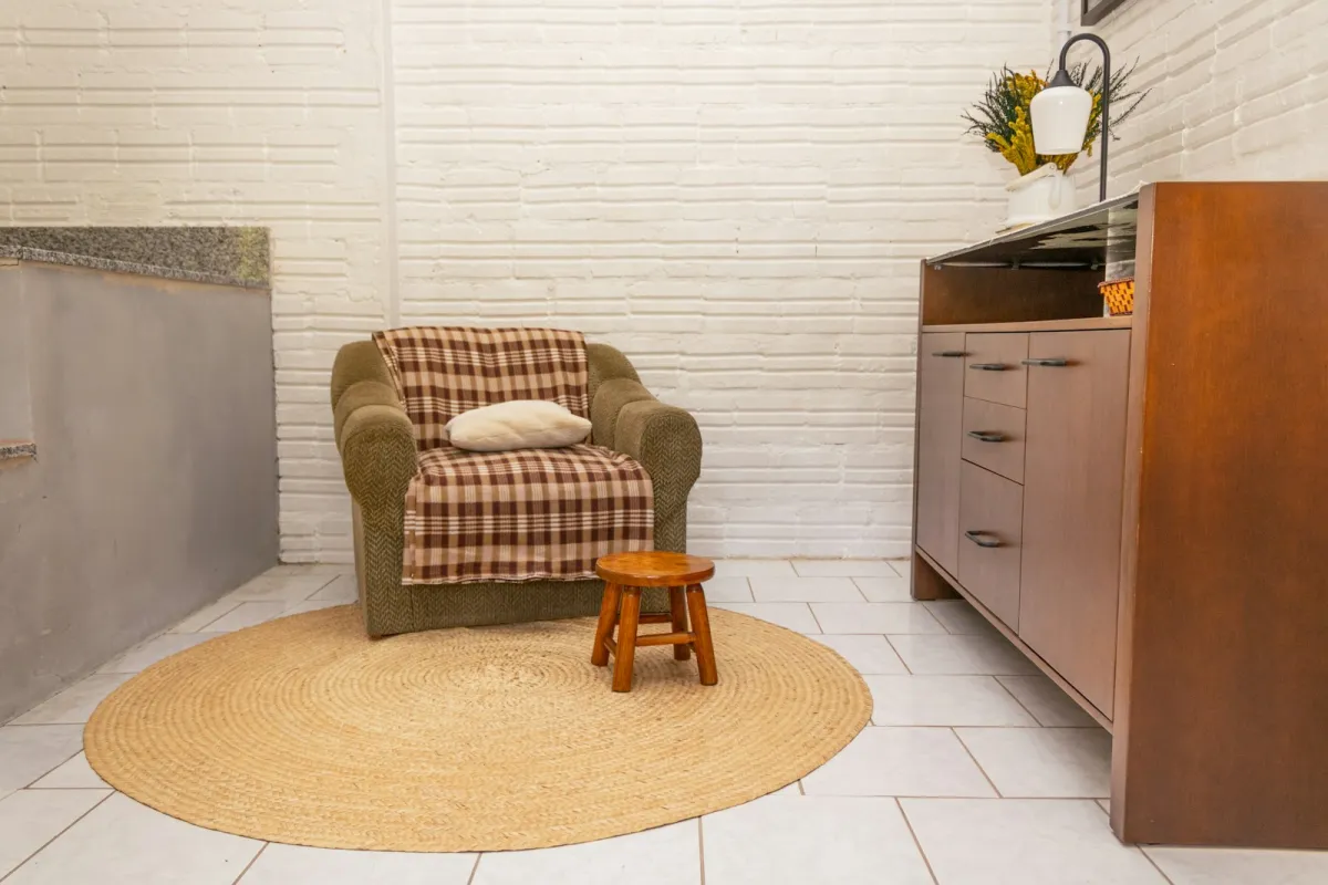 An armchair with a checked blanket and cushion beside a small wooden stool on a round rug