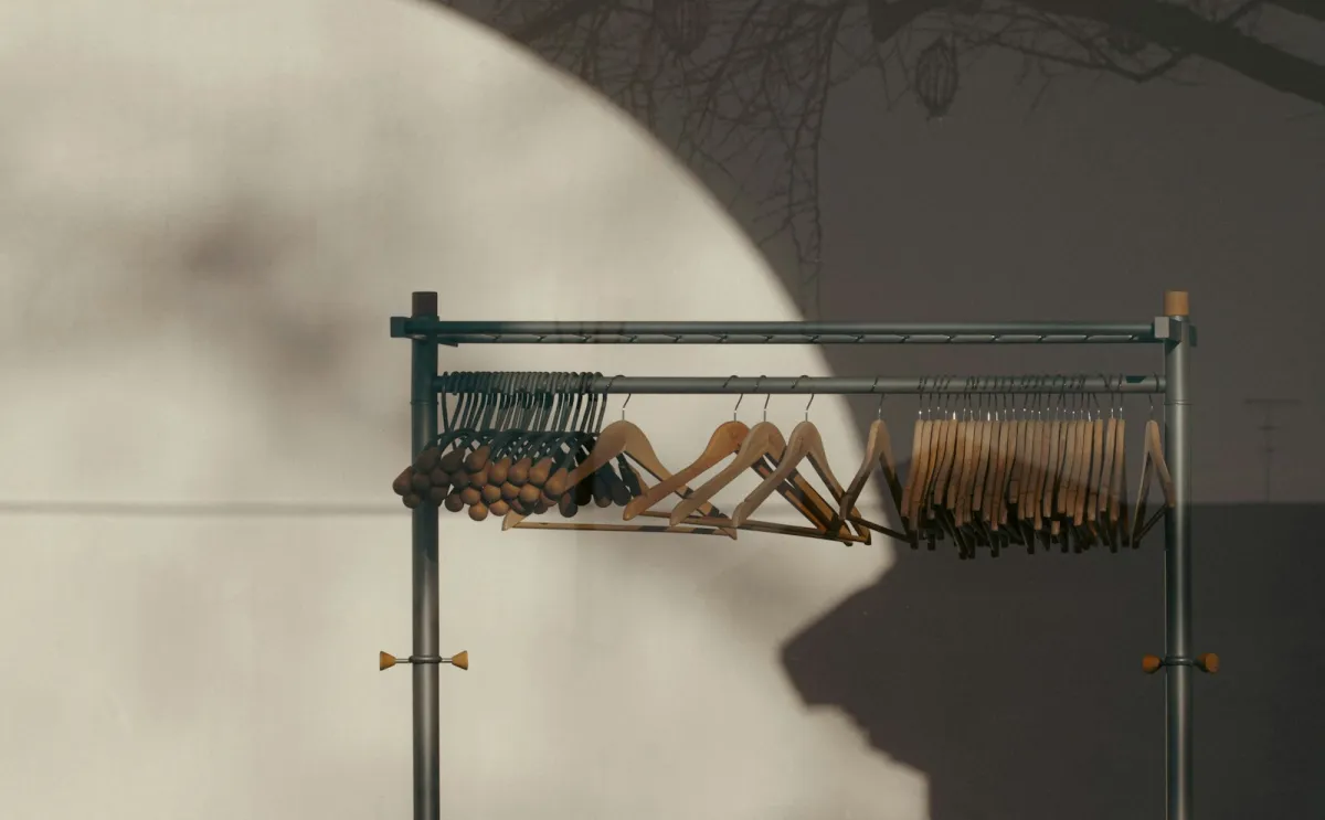 Wooden hangers on a metal clothes rail against a sunlit wall