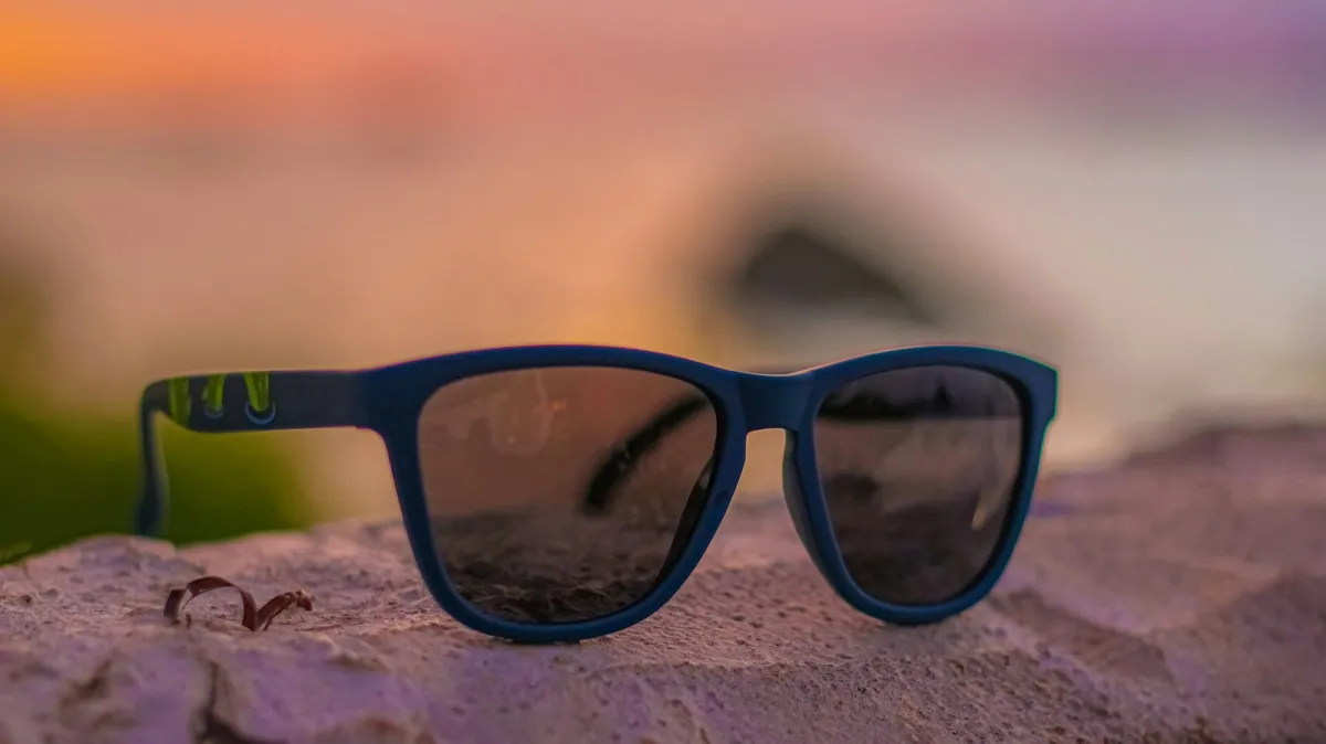 Blue-framed sunglasses resting on a rock at sunset Blue-framed sunglasses resting on a rock at sunset