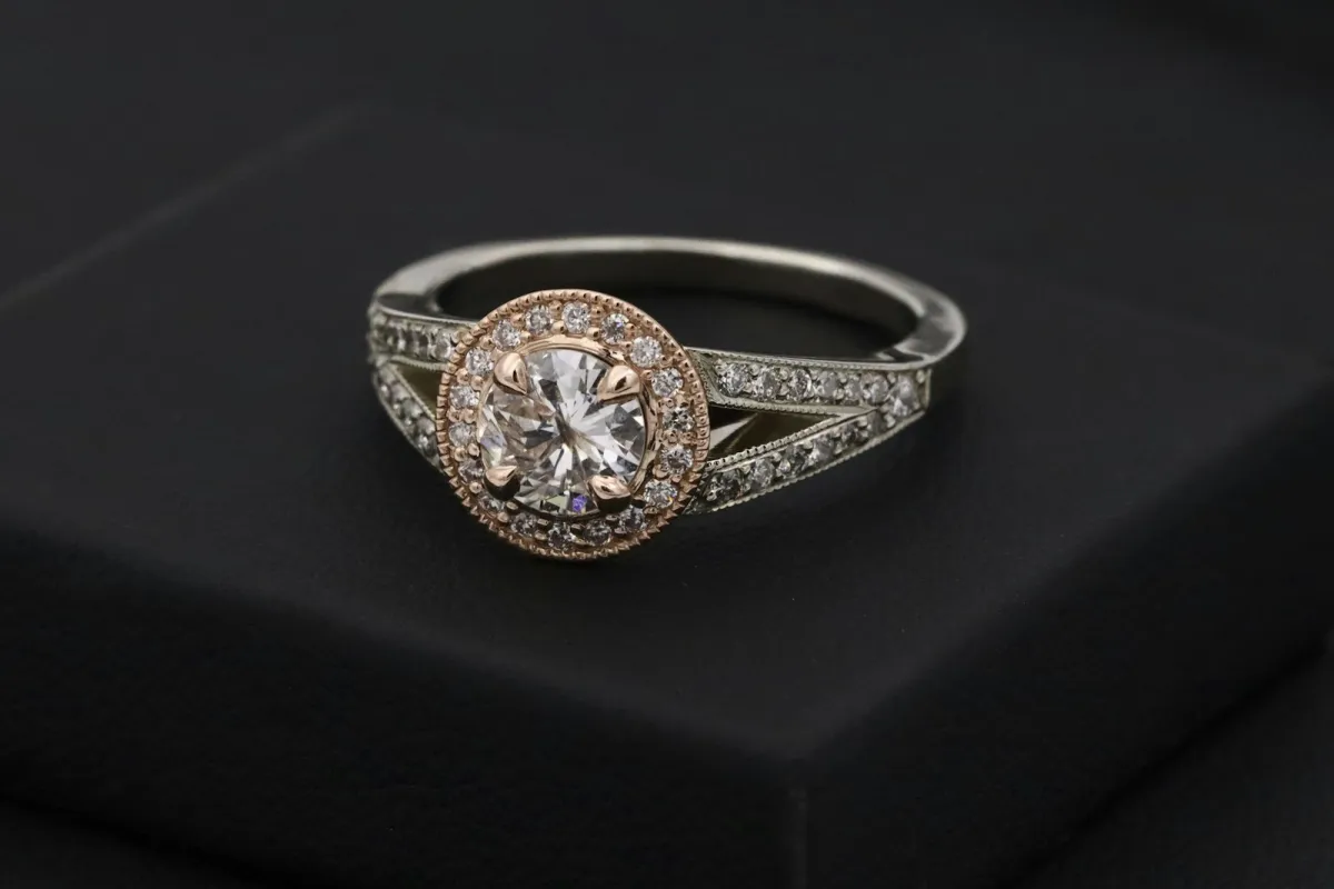 A diamond halo engagement ring in rose and white gold resting on a black box A diamond halo engagement ring in rose and white gold resting on a black box