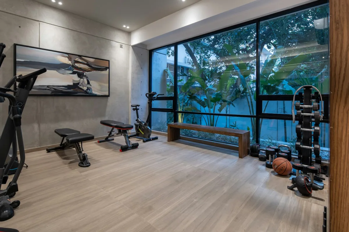 Home gym with an exercise bike, benches and dumbbells by a large window