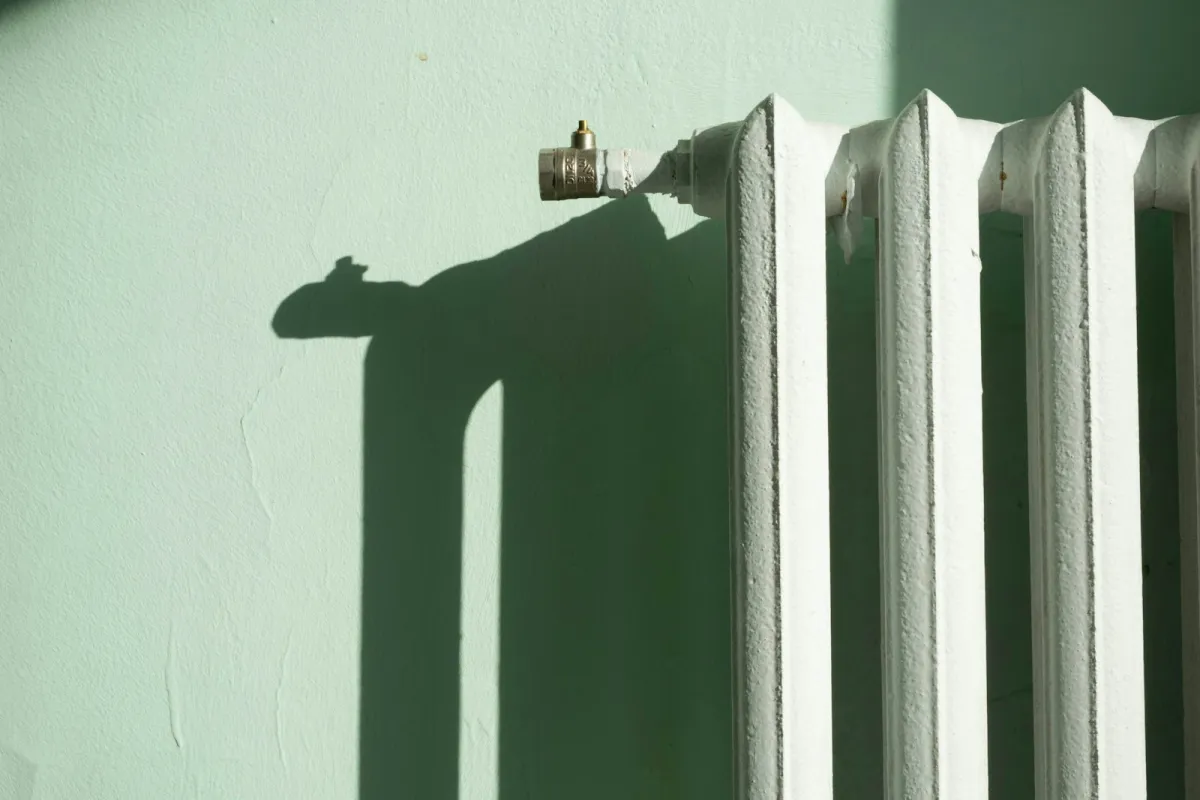 White cast iron radiator and valve against a pale green wall in winter sunlight White cast iron radiator and valve against a pale green wall in winter sunlight