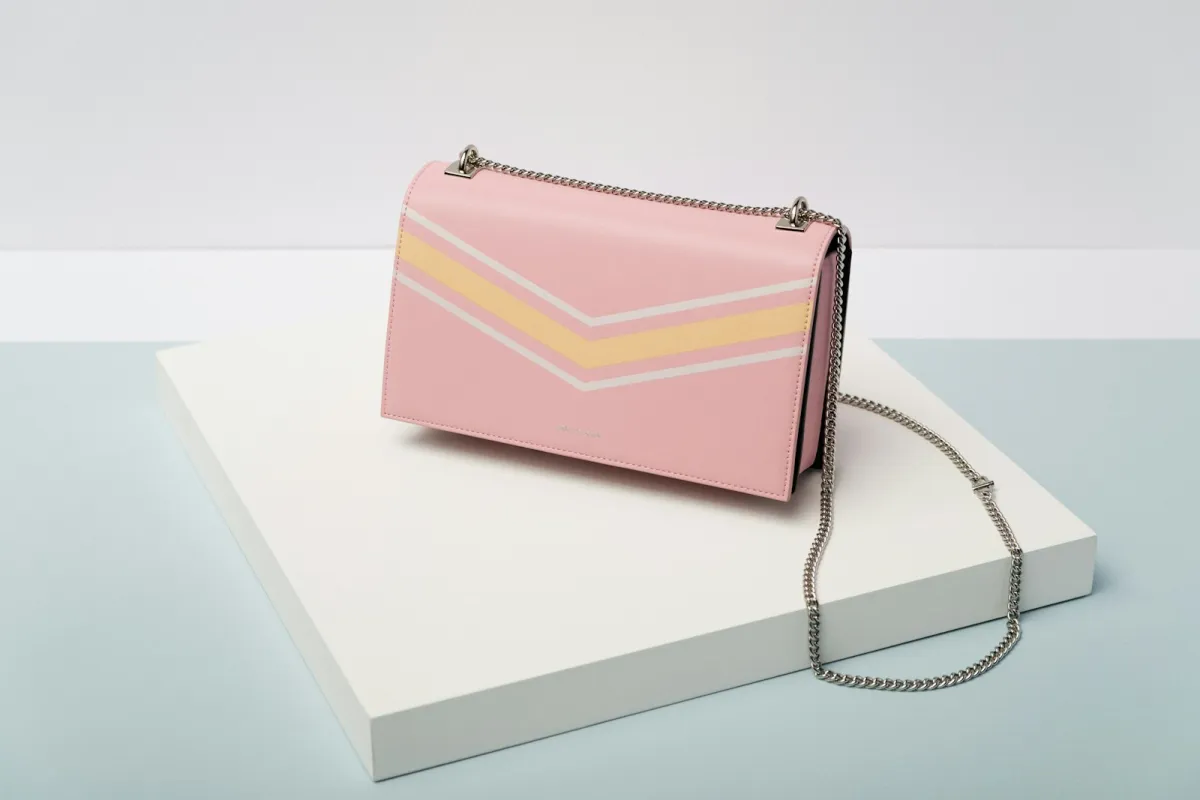 A pink leather crossbody bag with a silver chain strap on a white plinth