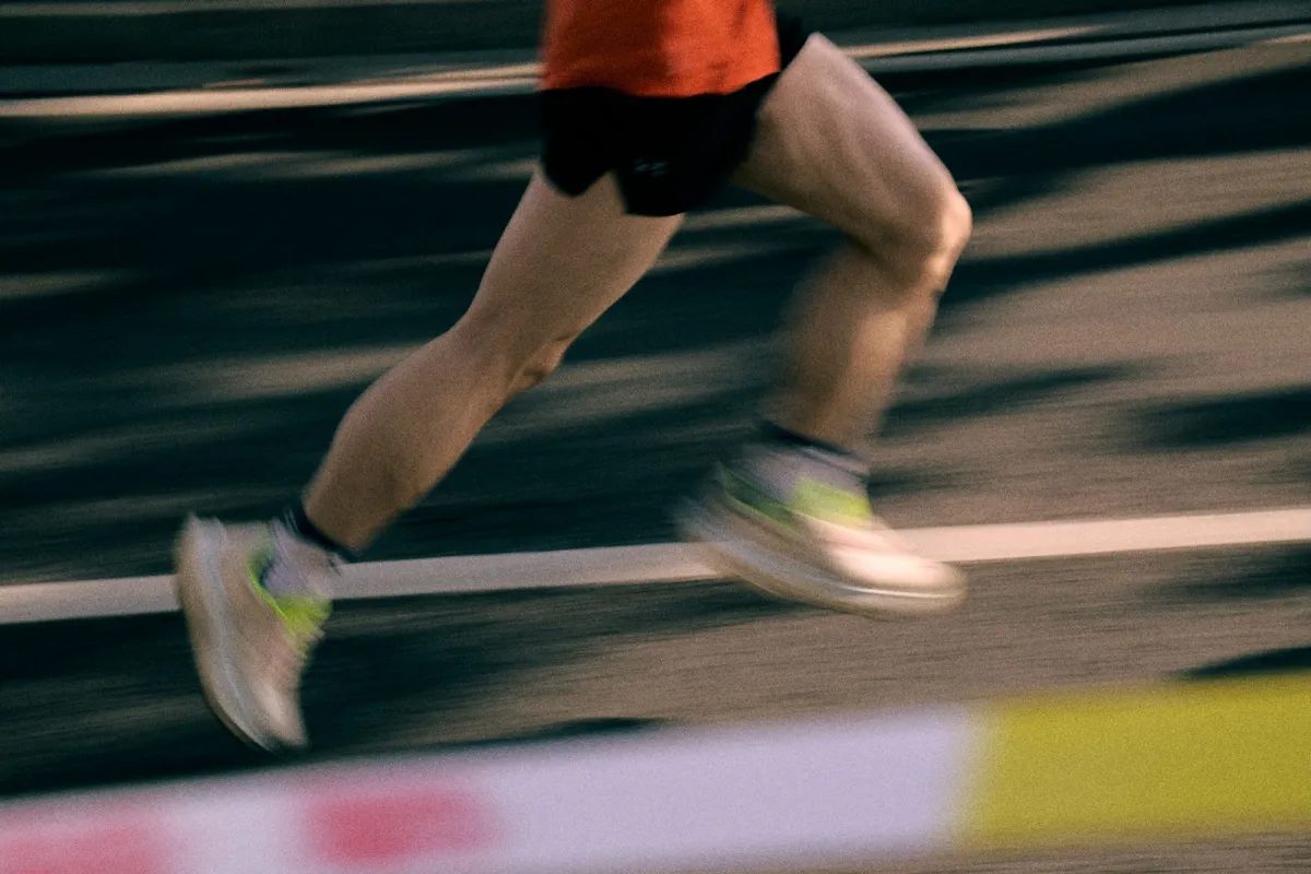 A runner's legs in motion on an athletics track, blurred with speed