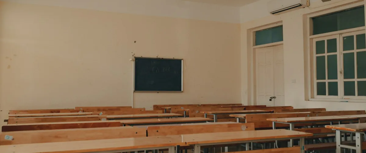 An empty classroom with rows of desks facing a chalkboard An empty classroom with rows of desks facing a chalkboard