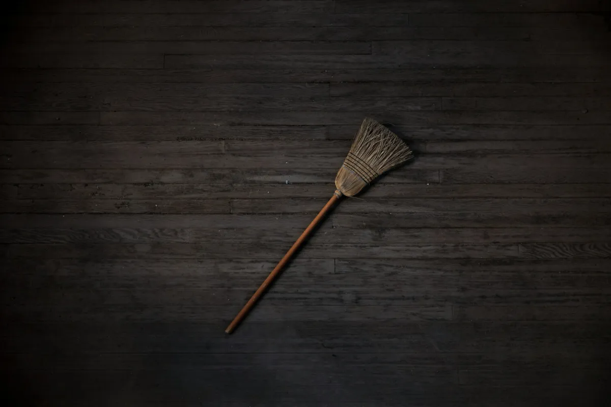 A traditional broom with a wooden handle lying on dark floorboards
