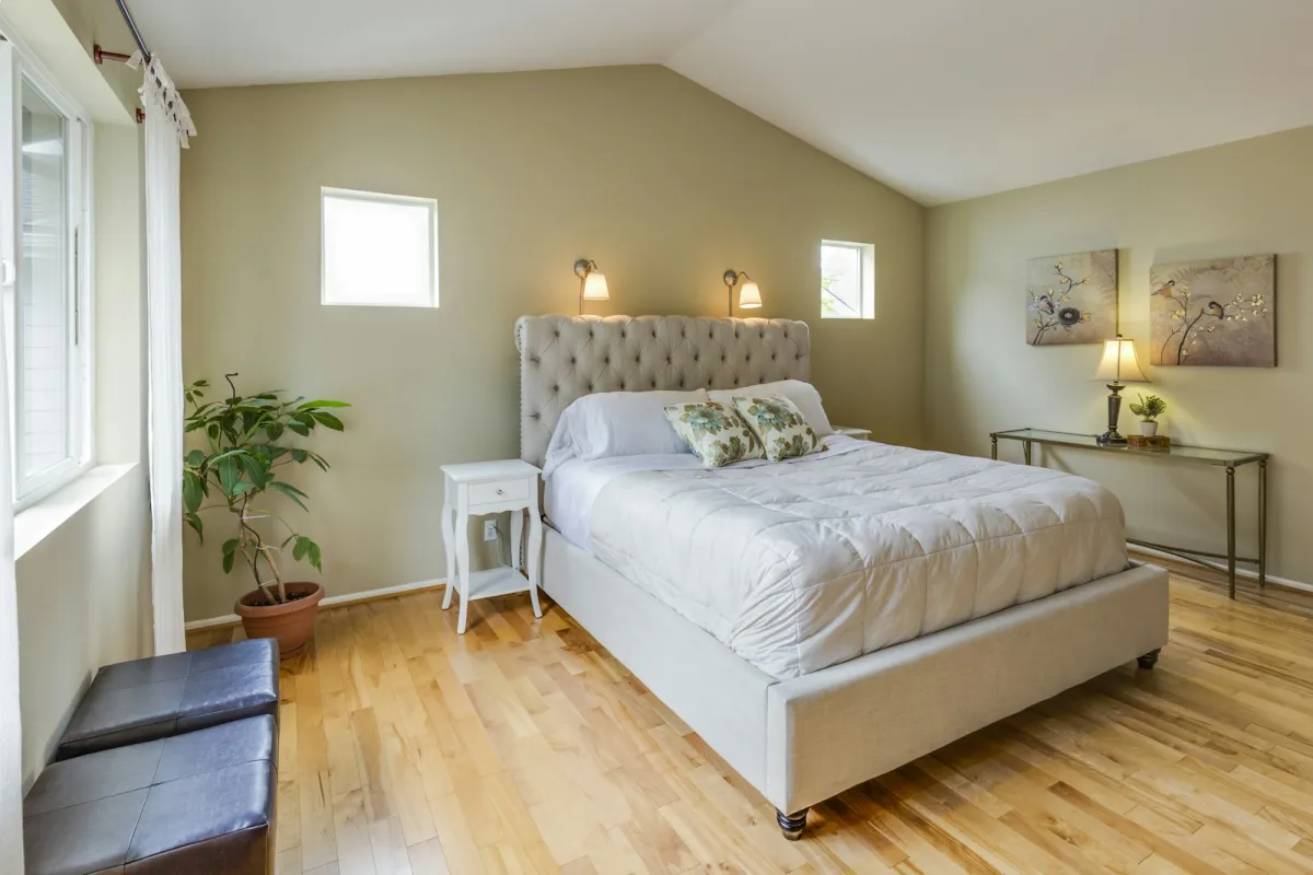 A tufted upholstered bed with white bedding in a bright bedroom with wooden floors A tufted upholstered bed with white bedding in a bright bedroom with wooden floors