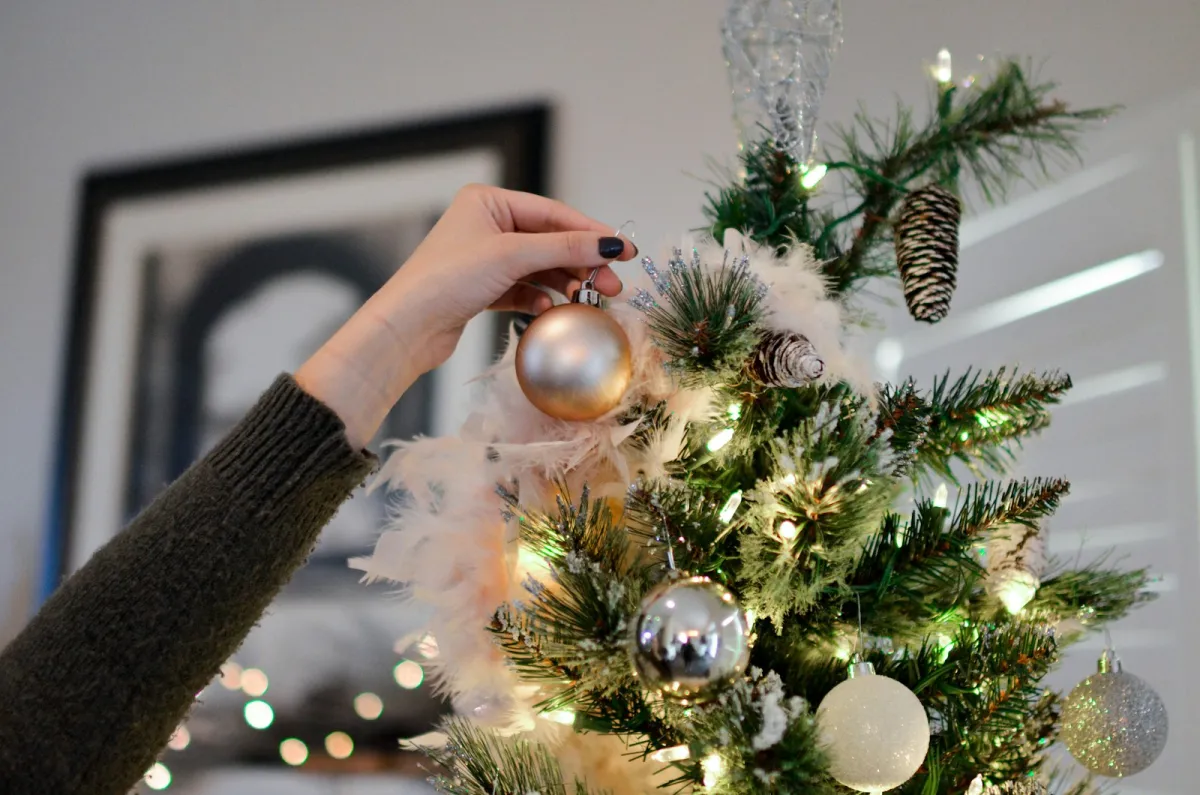 Hand hanging a gold bauble on a lit Christmas tree Hand hanging a gold bauble on a lit Christmas tree